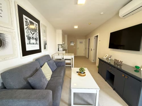 Moderno apartamento en Fuengirola con vistas al mar, sofá gris, TV de pantalla plana, mesa de comedor blanca y decoración contemporánea