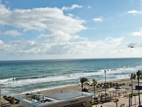 Apartamento en primera línea de playa en Fuengirola con vistas al mar, palmeras y playa de arena con olas