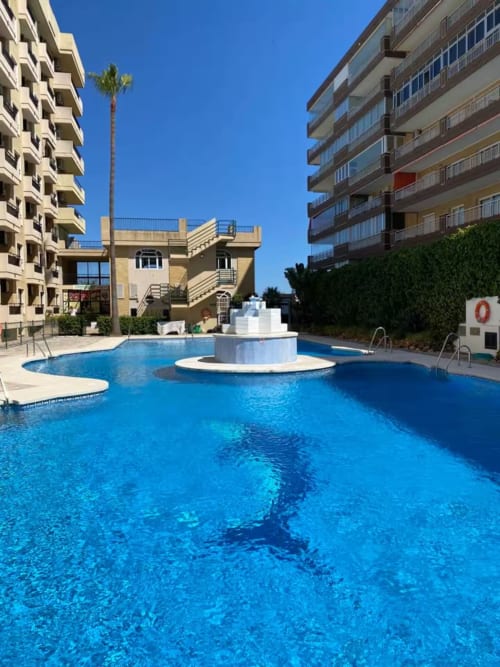 Piscina de apartamento frente al mar en Fuengirola con agua cristalina, fuente central y arquitectura mediterránea bajo cielo despejado