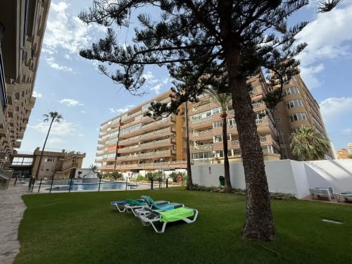 Jardín de apartamento frente al mar en Fuengirola con tumbonas, palmeras y vistas al Mediterráneo entre edificios de estilo mediterráneo