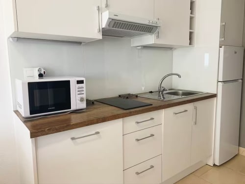 Cocina moderna y compacta con muebles blancos, encimera de madera, microondas, placa de cocción, fregadero y refrigerador en Fuengirola