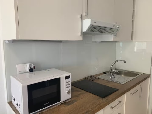 Pequeña cocina moderna en apartamento frente al mar, Fuengirola. Microondas blanco, placa de inducción, fregadero de acero inoxidable con grifo.