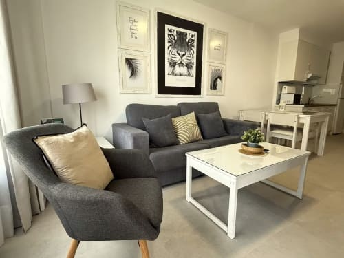 Sala de estar moderna en Fuengirola con sofá gris, sillón y cuadros con vistas al mar en las paredes