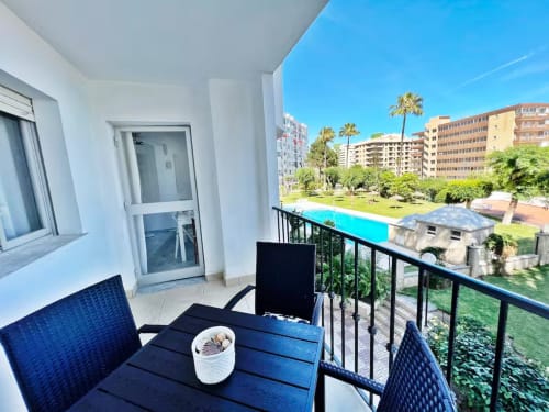 Balcón con vista a la piscina en apartamento beachfront de Fuengirola con palmeras y edificios residenciales