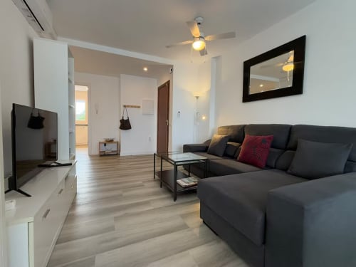 Moderna sala de estar en apartamento de playa en Fuengirola con sofá negro, TV y vistas a la piscina