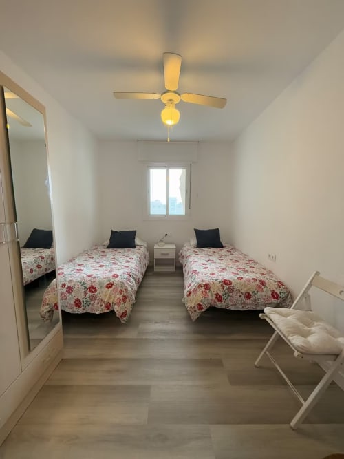 Luminoso dormitorio doble con ropa de cama floral, ventilador de techo y ventana en apartamento de playa en Fuengirola de Grupo Inmo House