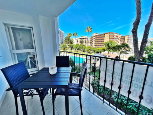 Soleado balcón con vistas a la piscina en apartamento de Fuengirola, muebles azules, palmeras y edificios costeros visibles