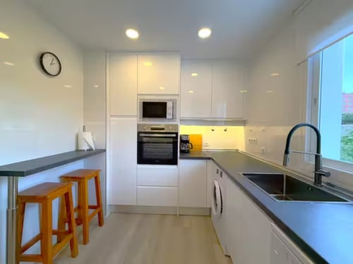 Cocina moderna blanca con barra, fregadero de acero inoxidable e iluminación amarilla en apartamento de playa en Fuengirola