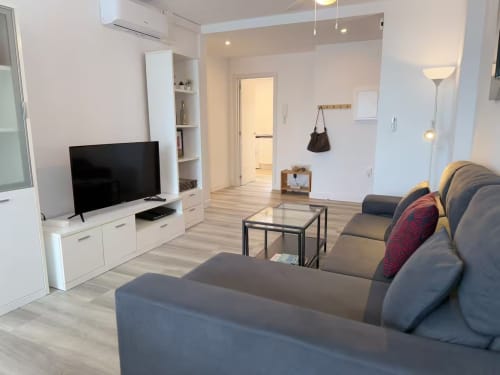 Moderna sala de estar en apartamento de playa de Fuengirola con sofá gris, televisión, suelos de madera y acceso a vista de piscina