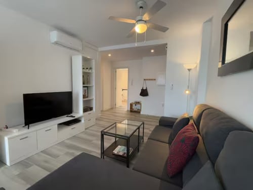 Sala de estar moderna en apartamento de playa en Fuengirola con sofá gris, televisor y vistas a la piscina