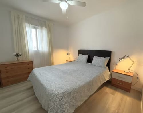 Dormitorio luminoso en apartamento de Fuengirola con vistas a piscina, cama, cómodas de madera e iluminación cálida