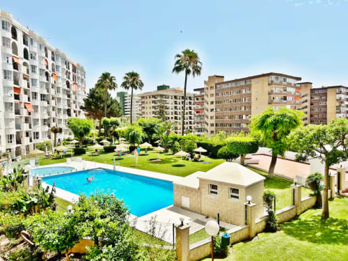Complejo de apartamentos en Fuengirola con piscina climatizada, palmeras, patio ajardinado y edificios modernos de varios pisos