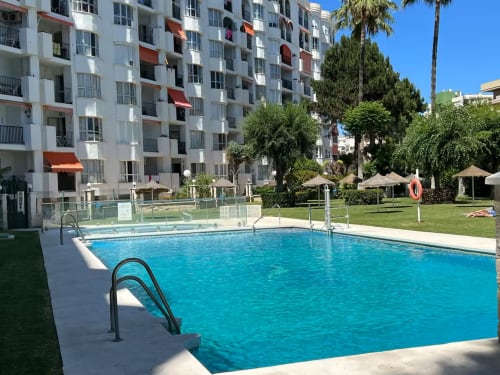 Piscina del apartamento en Fuengirola con tumbonas, palmeras y moderno edificio frente al mar en soleado patio