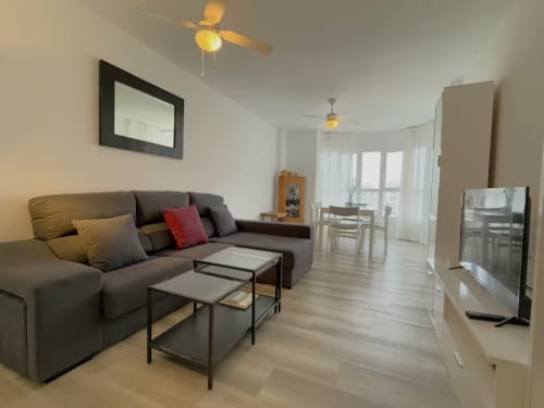 Moderno apartamento en la playa de Fuengirola con sofá gris, zona de comedor y vistas a la piscina desde el balcón