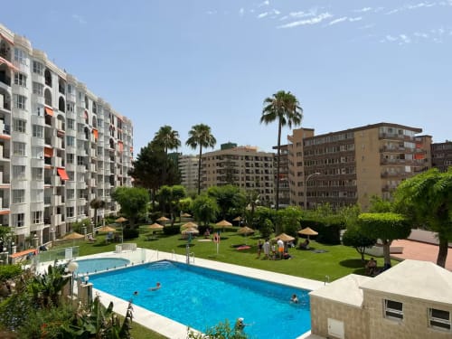 Vista soleada de la piscina en complejo de apartamentos frente al mar en Fuengirola con palmeras y jardines
