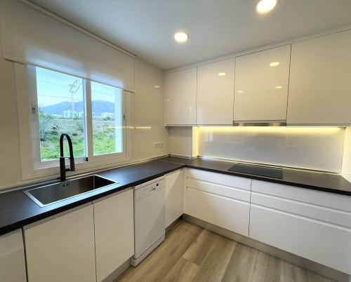 Cocina moderna en apartamento de playa en Fuengirola con muebles blancos, encimeras negras y vistas a la montaña