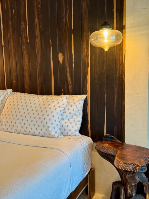 Recámara Villa Tulum en Ala Residencias, Chetumal con cabecera de madera oscura, lámpara colgante y mesita de noche rústica