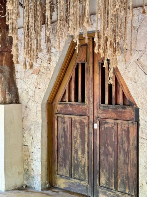 Puertas de madera rústica con detalles tallados en Ala Residencias Villa Tulum, Chetumal, con decoraciones de palma seca encima