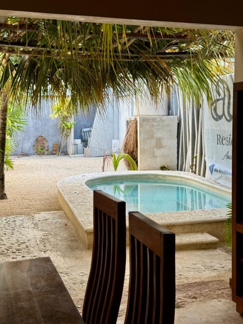 Zona de piscina tropical en Ala Residencias Villa Tulum en Chetumal con techo de palma y playa de arena
