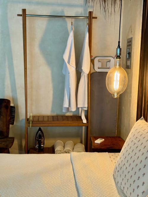 Perchero de madera con ropa de cama blanca y lámpara colgante en la habitación Villa La Guardia de Ala Residencias, Chetumal