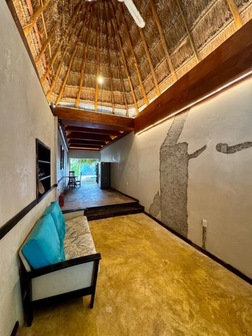 Interior de Villa La Guardia con techo de palapa, asientos turquesas y vista al jardín en Ala Residencias, Chetumal