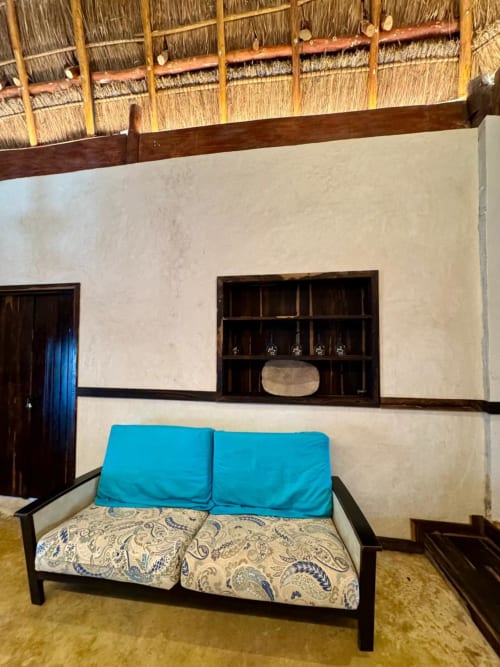 Acogedora habitación en Ala Residencias Chetumal con cama-diván acolchada en azul, estantería de madera y detalles de techo con materiales naturales.