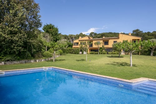 Villa de lujo en Palafrugell con piscina azul reluciente, jardín impecable y casa mediterránea amarilla rodeada de árboles