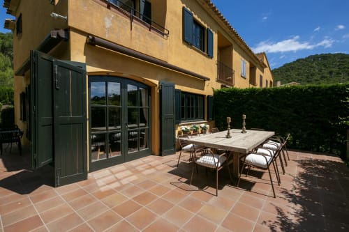 Terraza soleada de la villa La Pastora en Palafrugell con mesa de comedor, persianas verdes y vistas al paisaje mediterráneo