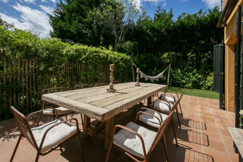 Mesa de comedor al aire libre con sillas en terraza de terracota en la villa Llafranc, rodeada de frondoso jardín y árboles