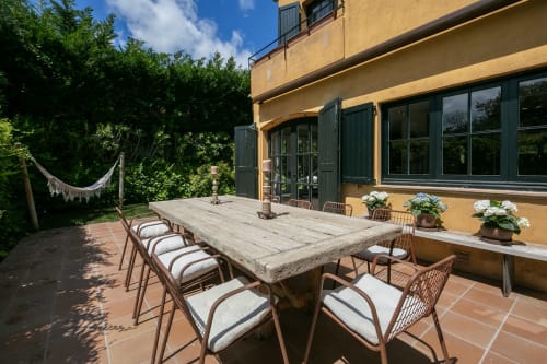 Terraza de comedor al aire libre de la villa Palafrugell con mesa de madera, sillas de mimbre y macetas de flores con vistas a los jardines