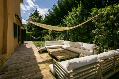 Terraza exterior de la villa Llafranc con tumbonas de madera, cojines crema, toldo de sombra y frondosos setos verdes en Palafrugell