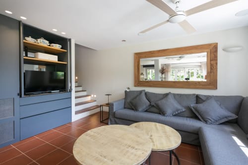 Sala de estar moderna en la villa La Pastora de Llafranc con sofá gris, espejo de madera, mueble TV y baldosas de barro