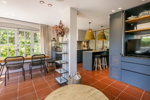 Cocina y comedor de villa moderna en Palafrugell con suelos de terracota, muebles azules, lámparas doradas y jardín