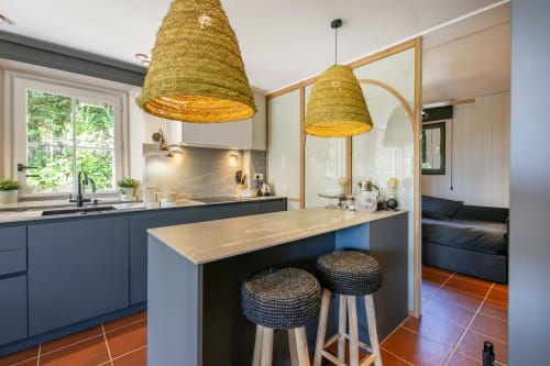 Cocina de villa moderna en Palafrugell con muebles azules, lámparas colgantes tejidas, isla central y suelo de terracota