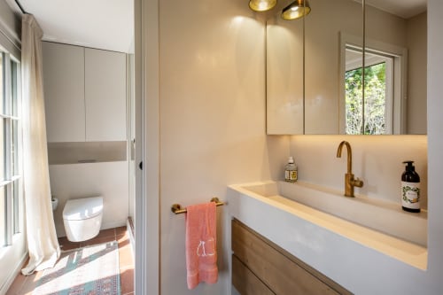 Baño moderno con lavabo, grifo dorado, gabinete espejado y zona de inodoro separada en la villa La Pastora en Palafrugell