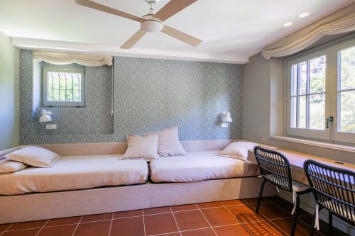 Dormitorio moderno en la villa La Pastora en Llafranc con cama tapizada rosa, paredes estampadas, ventilador de techo y grandes ventanas