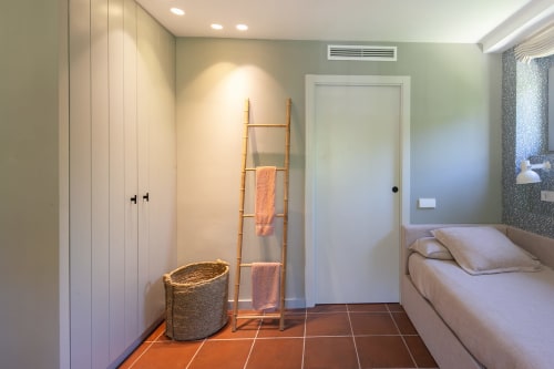 Dormitorio moderno con escalera de madera para toallas, cesta tejida, armario blanco y suelo de baldosas de barro en villa La Pastora