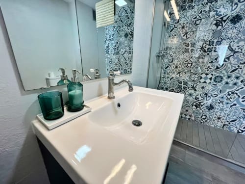 Moderno baño con lavamanos blanco, accesorios en tonos turquesa y azulejos decorativos con motivos azules en apartamento frente al mar en Fuengirola