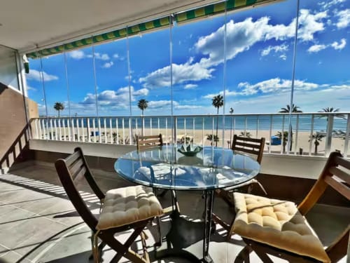 Balcón de apartamento frente al mar en Fuengirola con mesa de comedor de cristal, vistas al océano, palmeras y playa de arena