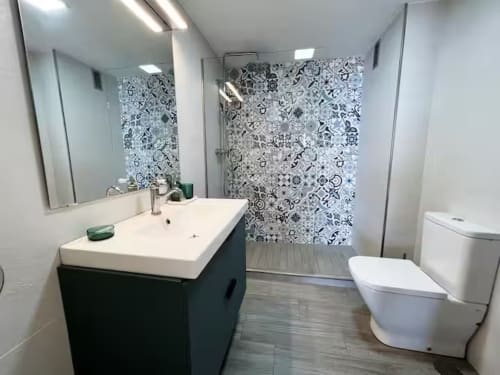 Baño moderno con tocador negro, lavabo blanco, azulejos decorados en ducha e inodoro en Grupo Inmo House Fuengirola