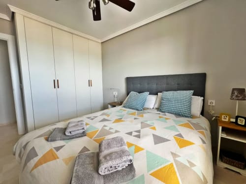 Dormitorio moderno en apartamento frente al mar en Fuengirola con ropa de cama de patrón geométrico, cabecero gris, armarios blancos y vistas al mar