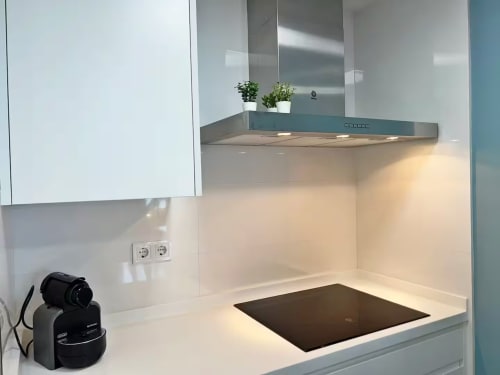 Moderna cocina con campana extractora de acero inoxidable, placa de cocción negra y gabinetes blancos en apartamento frente al mar