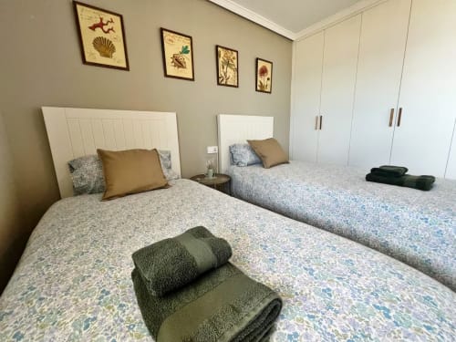 Moderno dormitorio doble en apartamento frente al mar en Fuengirola con vistas al océano, cabeceros blancos y toallas verdes dobladas