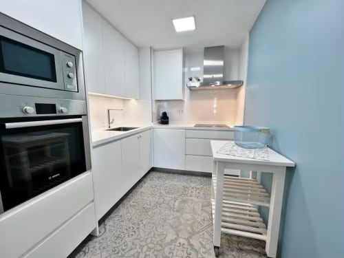 Cocina blanca moderna en apartamento frente al mar de Grupo Inmo House Fuengirola con electrodomésticos de acero inoxidable y azul claro