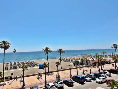 Vista de la playa de Fuengirola frente al mar con palmeras, arena, coches estacionados y Mar Mediterráneo