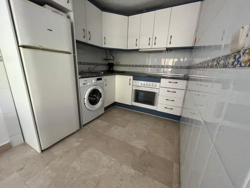 Moderna cocina en apartamento de Fuengirola con armarios blancos, lavadora, horno y suelo de baldosas beige