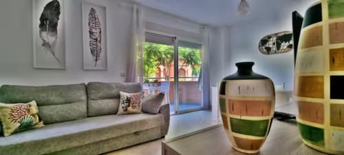 Salón moderno de apartamento en Fuengirola con sofá verde, plumas decorativas, jarrón de cerámica colorido, estanterías y terraza