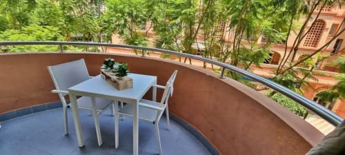Balcón moderno con mesa de comedor y sillas con vistas a exuberante vegetación y edificios de terracota en Fuengirola