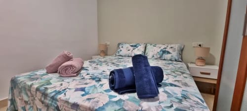 Acogedor dormitorio de apartamento frente al mar en Fuengirola con ropa de cama floral, toallas enrolladas y mobiliario moderno