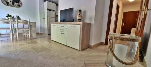 Moderno salón en Fuengirola con muebles blancos, televisor de pantalla plana y vistas a la ciudad, Grupo Inmo House
